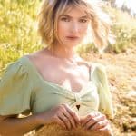 Blonde wavy wig styled on a woman outdoors with sunlight and greenery.